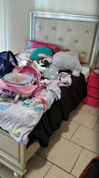 A child's bed buried under clothes, bags and toys
