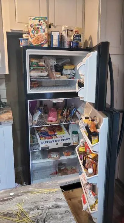 An open refrigerator packed with food, with spills on the shelves
