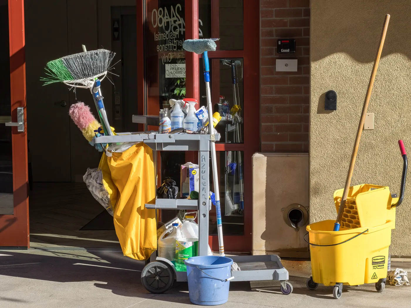 Stock photo of a cleaning cart with a mop bucket and supplies outside a building entrance